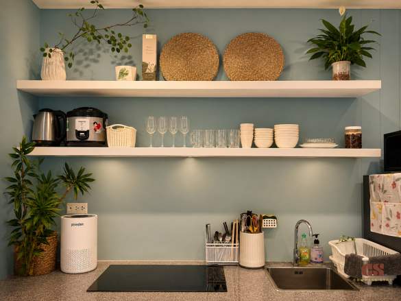 Compact kitchenette at Compass Stay with electric stove, sink, shelves, cookware, and tableware for long-stay guests.