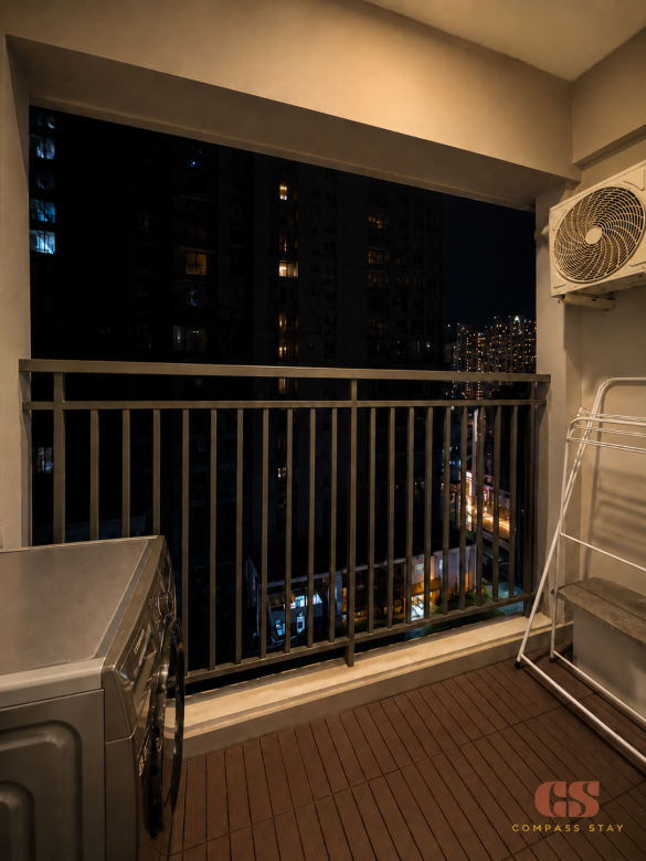 Private balcony laundry area at Compass Stay with washing machine, drying rack, and city building view.