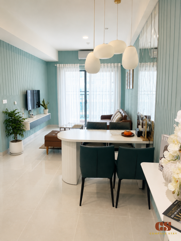 Modern living room at Compass Stay with leather sofa, dining table, teal wall, plants, and soft natural light.